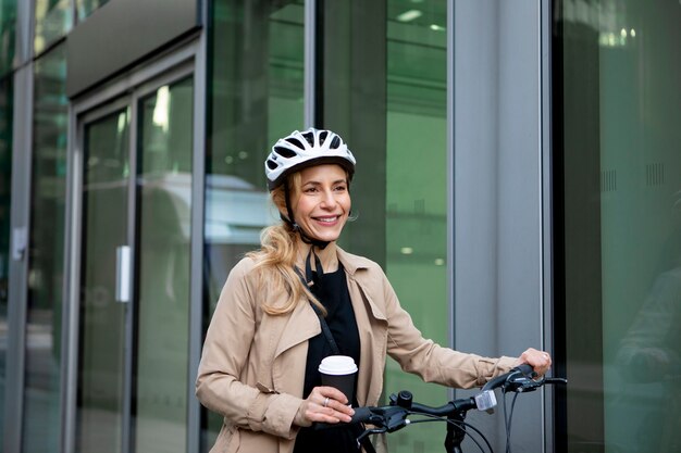 Mulher andando de bicicleta usando o capacete e segurando uma xícara de café