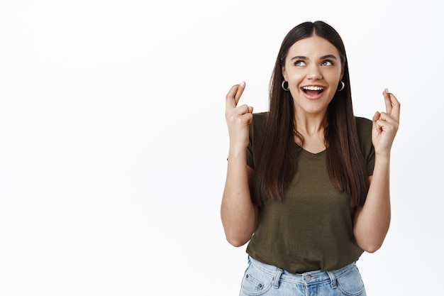 Mulher animada e esperançosa fazendo seu pedido, cruze os dedos para dar sorte, ofegando e olhando para o canto superior esquerdo