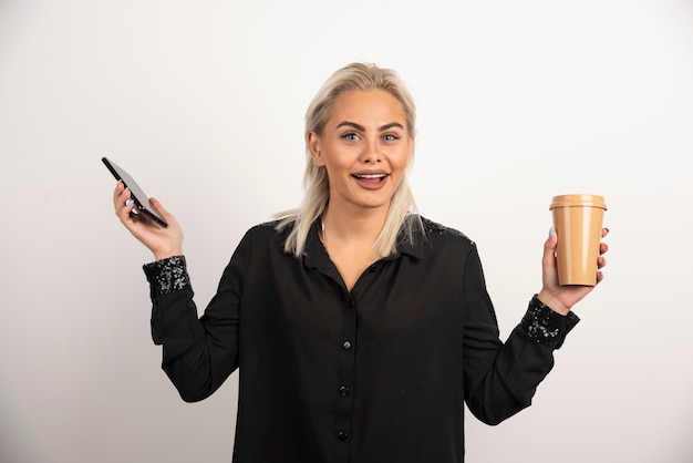 Mulher animada, posando com o celular e a xícara de café. Foto de alta qualidade