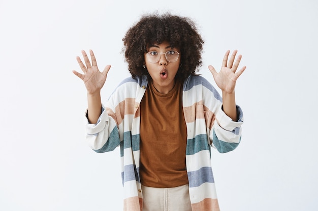 Mulher animada, sociável e criativa com um penteado afro levantando as palmas das mãos e dobrando os lábios, contando uma história assustadora durante uma viagem com amigos sentados perto do fogo, sendo persuasiva e emotiva