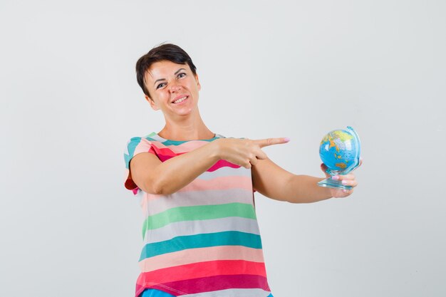 Mulher apontando para o globo do mundo em t-shirt listrada e parecendo decepcionada. vista frontal.