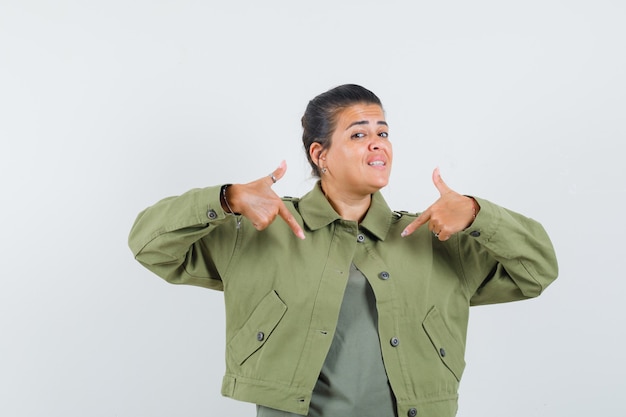 Mulher apontando para si mesma em jaqueta, camiseta e parecendo confiante.