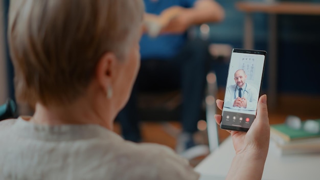 Mulher aposentada participando de consulta on-line em videochamada com médico, falando sobre cuidados de saúde. Adulto sênior usando videoconferência online com médico para telemedicina e telessaúde.