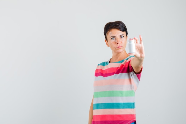 Mulher apresentando frasco de comprimidos em camiseta listrada e olhando com cuidado