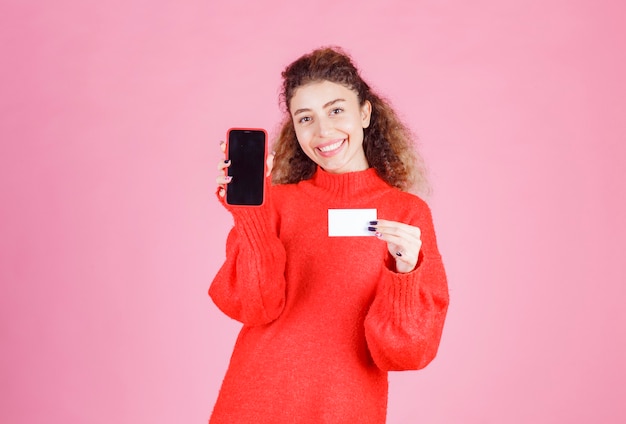 Mulher apresentando seu cartão de visita e mostrando seu telefone com a intenção de entrar em contato.