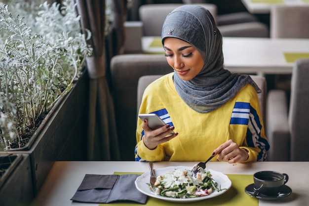 Mulher árabe em hijab dentro de um café comendo salada