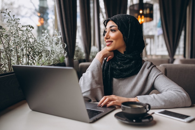 Mulher árabe em hijab dentro de um café trabalhando no laptop