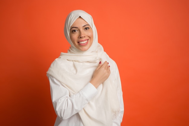 Mulher árabe feliz em hijab. Retrato de menina sorridente, posando no fundo vermelho do estúdio. Mulher jovem e emocional. As emoções humanas, o conceito de expressão facial. Vista frontal.