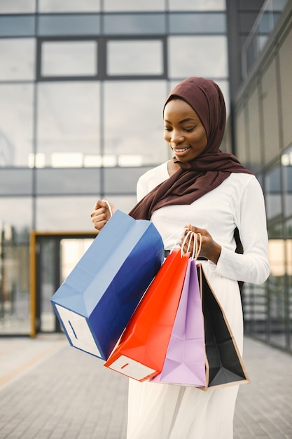 Mulher árabe usando hijab em pé com sacolas de compras perto de shopping