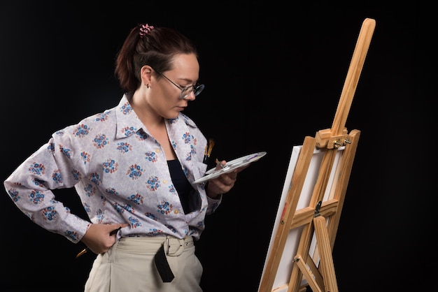 Mulher artista segurando uma escova e olhando para uma tela em fundo preto