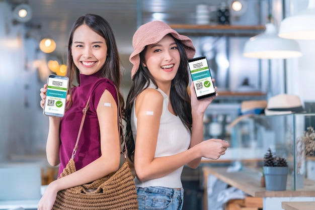 Mulher asiática alegre sorridente adolescente ponto de gesto de mão mostrar marca de vacina contra covid19 e passaporte de vacina digital da tela do smartphone depois de receber a vacina prevenir o conceito de saúde