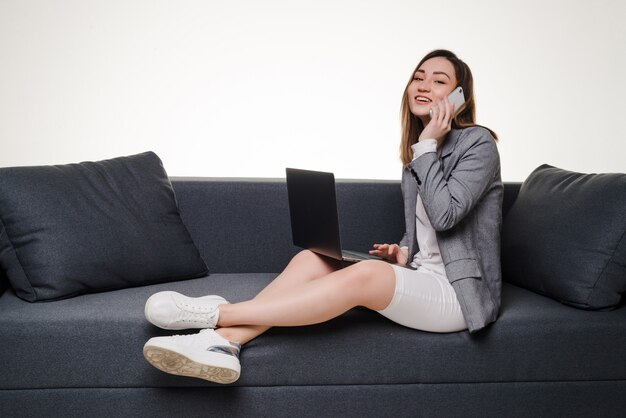 Mulher asiática ao telefone usando o laptop em casa na sala de estar. Trabalhar em casa em regime de quarentena.