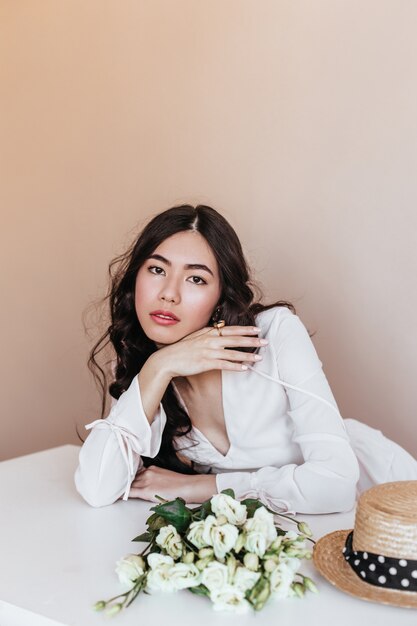 Mulher asiática atraente com flores brancas, olhando para a câmera. Foto de estúdio de uma mulher chinesa atraente com buquê de eustomas.