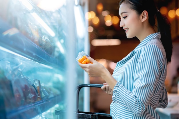 Mulher asiática atraente comprando com felicidade e alegre no supermercado borrão fundo bokeh do shopping jovem mulher asiática com carrinho de compras para produtos frescos