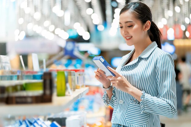 Mulher asiática atraente comprando com felicidade e alegre no supermercado borrão fundo bokeh do shopping jovem mulher asiática com carrinho de compras para produtos frescos