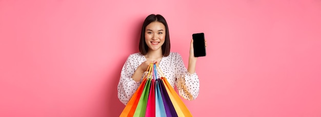 Mulher asiática atraente mostrando aplicativo de smartphone e sacolas de compras online via aplicativo standi