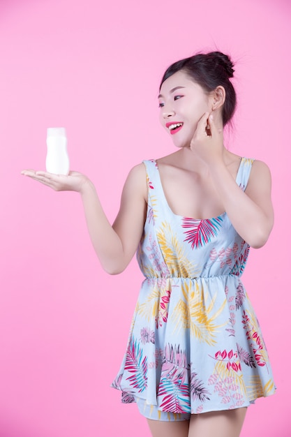 Mulher asiática bonita que guarda uma garrafa do produto em um fundo cor-de-rosa.