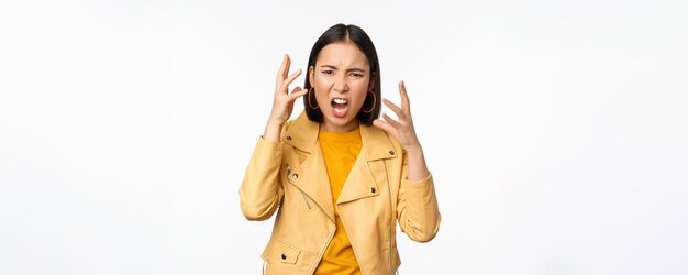 Mulher asiática com raiva discutindo apertando as mãos com raiva e gritando gritando com rosto frustrado sobre fundo branco