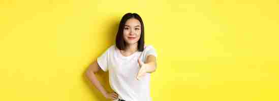 Foto grátis mulher asiática confiante em camiseta branca estende a mão para aperto de mão e gesto de saudação dizendo hel