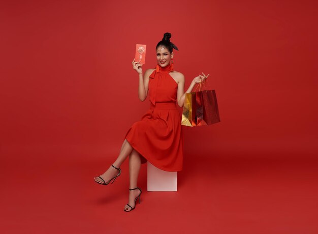 mulher asiática de vestido vermelho segurando sacos de compras e voucher de presente para compras de ano novo chinês