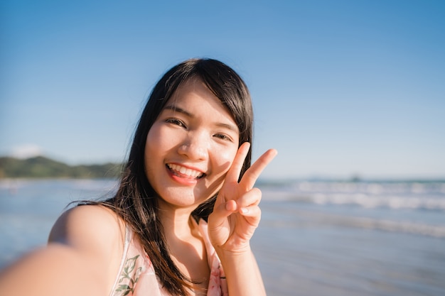Mulher asiática do turista na praia, fêmea bonita nova feliz sorrindo usando o telefone móvel que toma o selfie