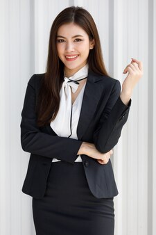 Mulher asiática em pé com metade do comprimento em um terno preto. empresária, segurando no terno formal de negócios em pé na sala de escritório. conceito mulher de trabalho bonita e confiante.