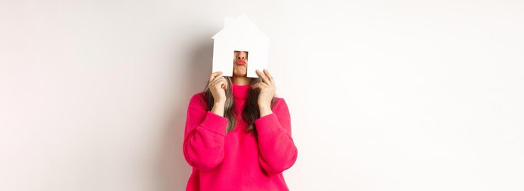 Foto grátis mulher asiática engraçada de meia-idade imobiliária escondendo o rosto atrás do modelo de casa de papel e mostrando l enrugado