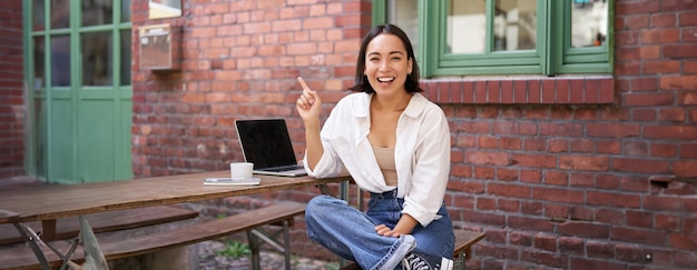 Mulher asiática entusiasmada apontando para o canto superior direito mostrando notícias publicitárias em banner olhando