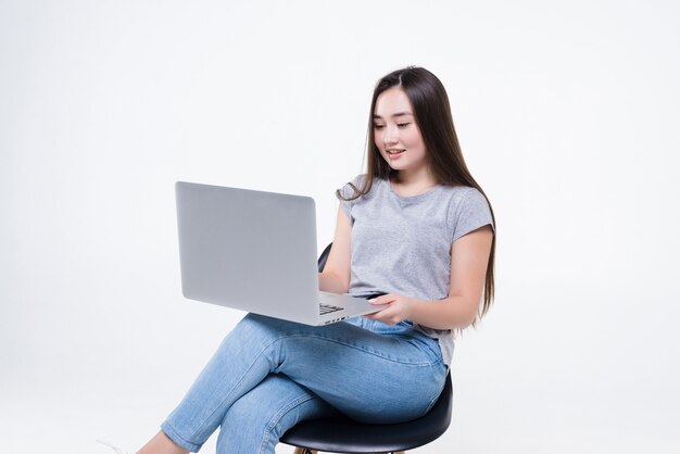 Mulher asiática falando ao telefone e olhando para um laptop enquanto está sentado em uma cadeira. Uma mulher trabalhadora estava sentada com as pernas cruzadas com confiança.
