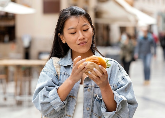 Mulher asiática feliz comendo um hambúrguer ao ar livre