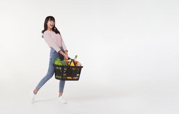 Mulher asiática feliz segurando cesta de compras cheia de legumes e tiro de estúdio de mantimentos