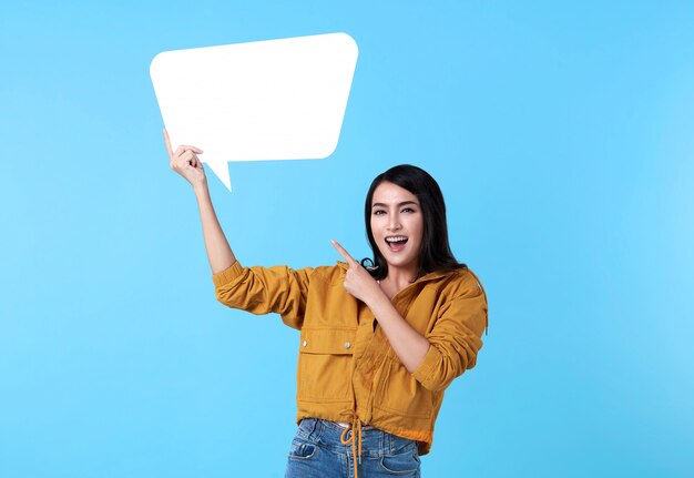 Mulher asiática feliz sorridente segurando balão em branco e com espaço vazio para texto em fundo azul.