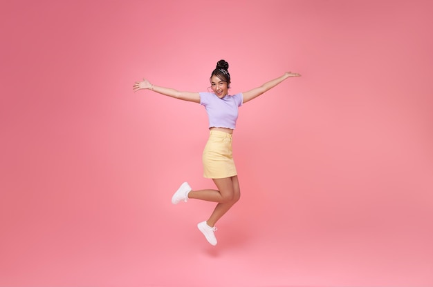 Foto grátis mulher asiática feliz sorrindo e pulando enquanto comemora o sucesso isolado sobre fundo rosa