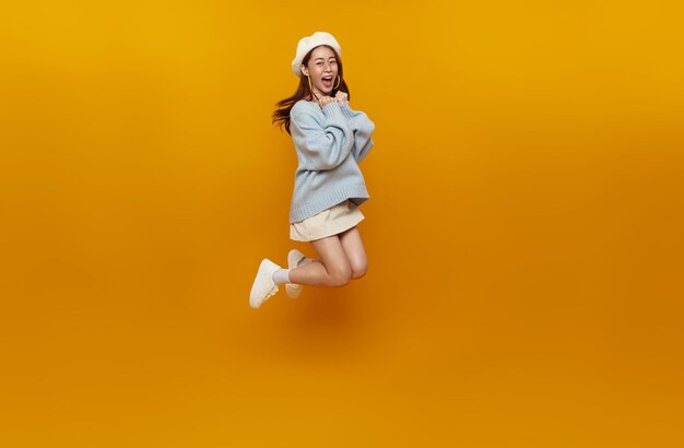 Mulher asiática feliz sorrindo e pulando enquanto comemorava o sucesso isolado sobre fundo amarelo