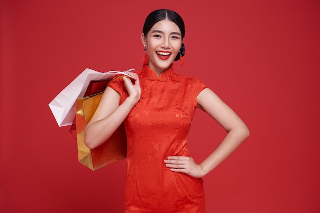 Mulher asiática feliz, viciada em compras, usando o vestido tradicional cheongsam qipao segurando uma sacola de compras