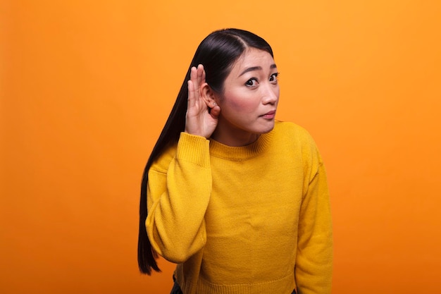 Mulher asiática morena curiosa escutando fofocas interessantes e rumores secretos sobre ela. Pessoa séria intrigada com a mão no ouvido ouvindo pessoas fofocando com interesse.