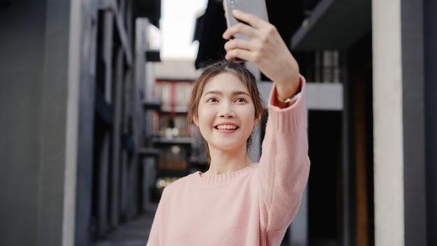 Mulher asiática nova bonita alegre do blogger do mochileiro que usa o smartphone que toma o selfie ao viajar no bairro chinês no pequim, china.