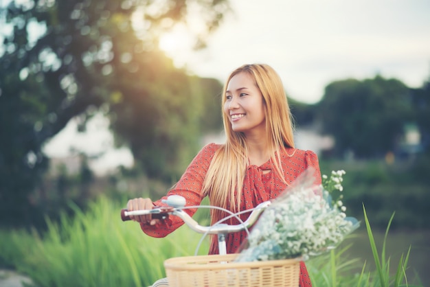 Mulher asiática nova bonita que monta uma bicicleta em um parque