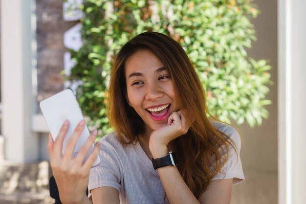 Mulher asiática nova feliz bonita atrativa que toma um selfie usando um telefone esperto no café
