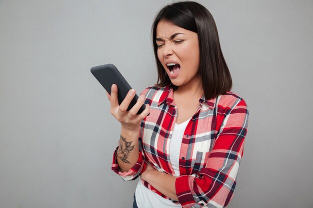 Mulher asiática nova irritada isolada usando o telefone.