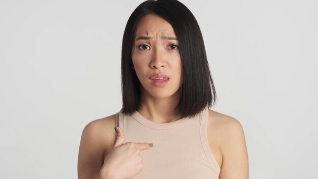 Mulher asiática parecendo indignada indicando-se isolada no fundo branco Expressão descontente
