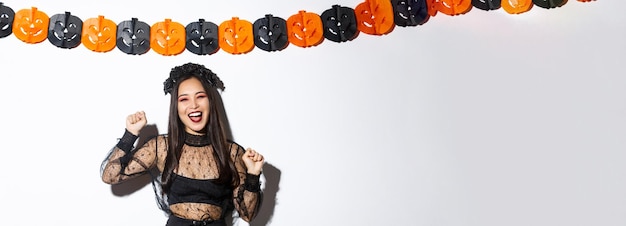 Foto grátis mulher asiática sorridente despreocupada em fantasia de bruxa curtindo festa de halloween dançando e regozijando-se em pé