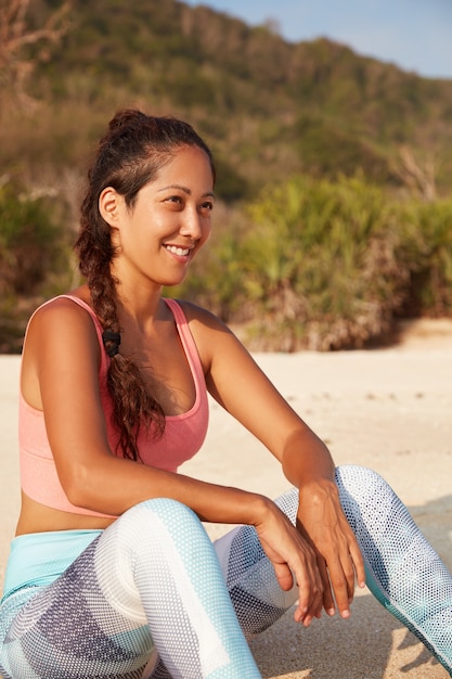 Mulher asiática sorridente e satisfeita com uma trança longa e escura, vestida com roupas esportivas