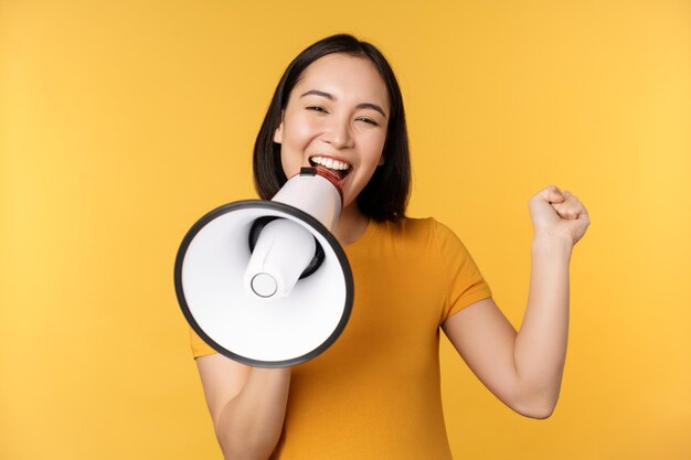 Mulher asiática sorridente em pé com megafone anunciando produto de publicidade smth sobre fundo amarelo