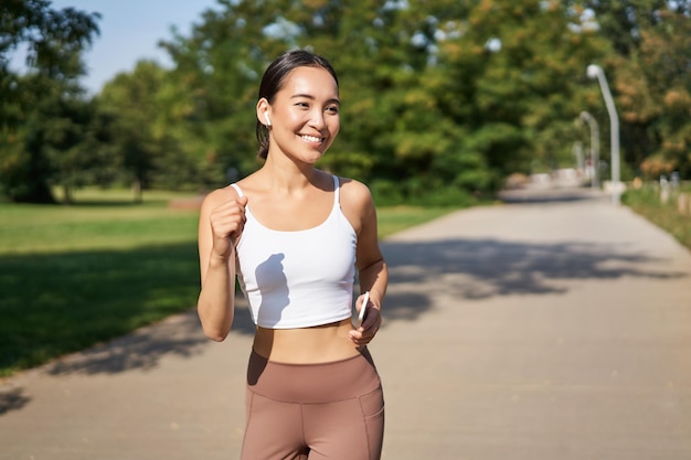 Mulher asiática sorridente feliz correndo no parque jovem corredor feminino saudável fazendo exercícios ao ar livre correndo