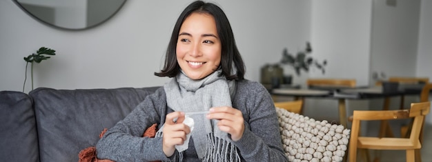 Foto grátis mulher asiática sorridente segurando termômetro e parecendo satisfeita, sentindo-se melhor depois que o resfriado se livrou