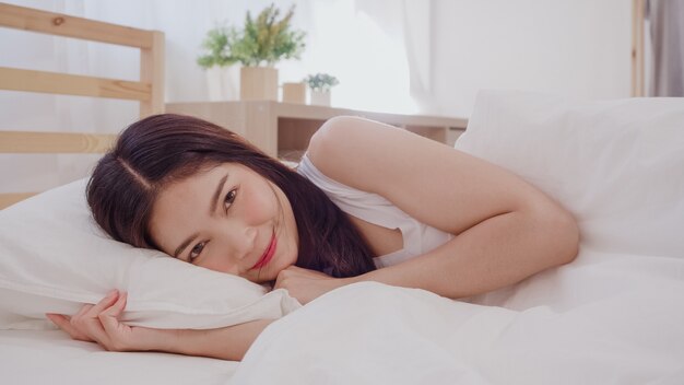 Mulher asiática sorrindo deitada na cama no quarto