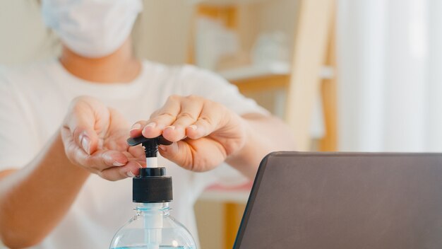 Mulher asiática usando álcool gel desinfetante para as mãos lavar a mão antes de abrir o laptop para proteger o coronavírus. Mulheres pressionam o álcool para limpar a higiene quando o distanciamento social fica em casa e o tempo de quarentena