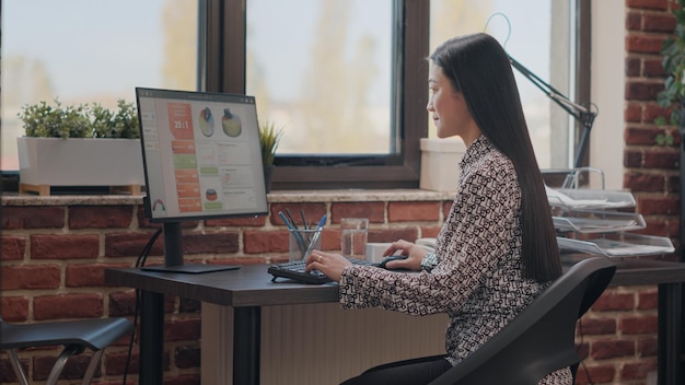 Mulher asiática usando computador para planejar a estratégia de negócios no escritório de inicialização. Funcionário da empresa trabalhando com design de gráficos para criar projeto financeiro para desenvolvimento de empregos. Empreendedor no trabalho