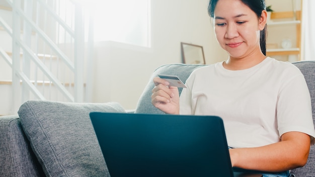 Mulher asiática usando laptop, cartão de crédito, compra e compra de comércio eletrônico na internet na sala de estar em casa